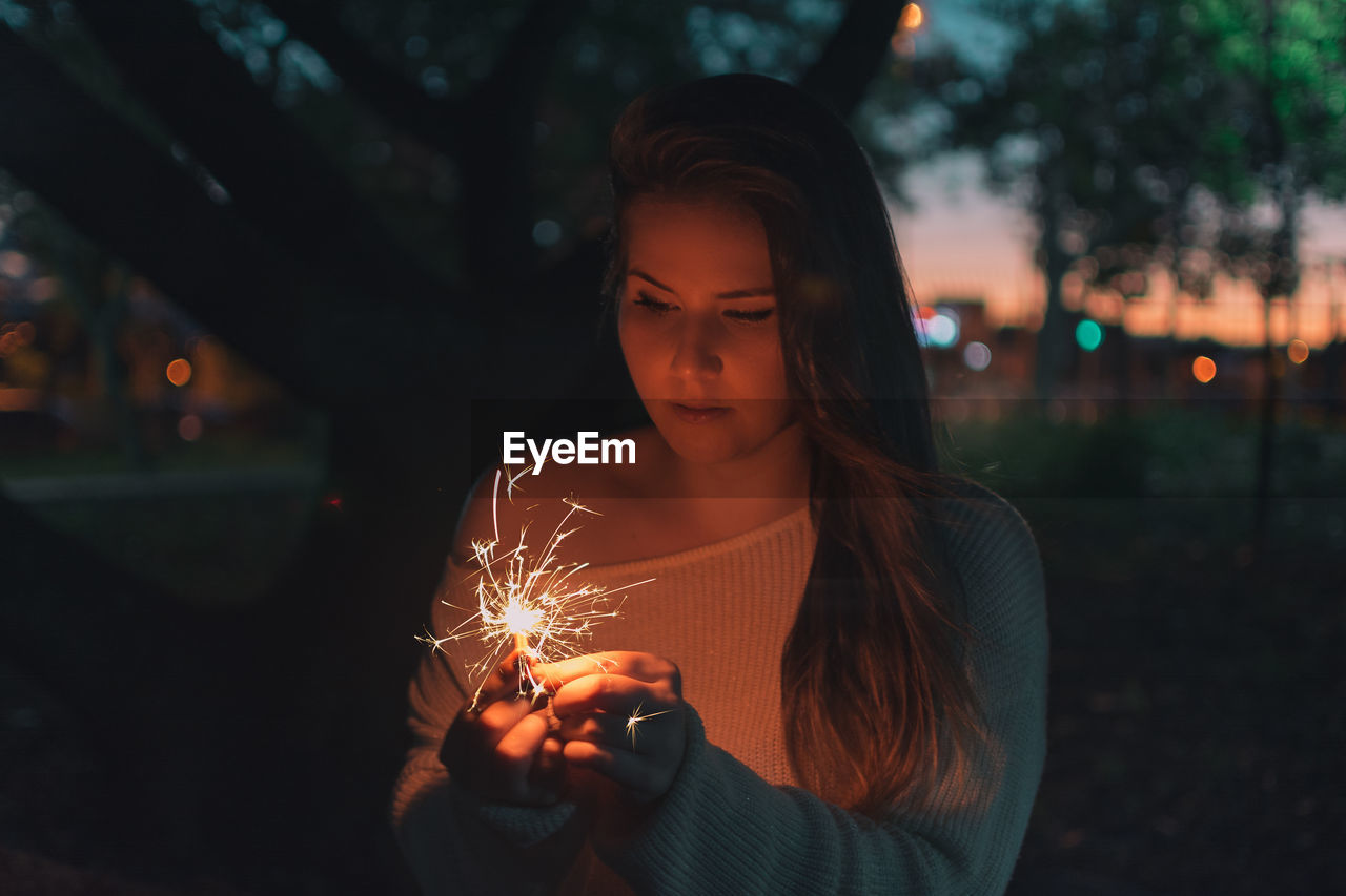 Young woman holding illuminated sparkler at night