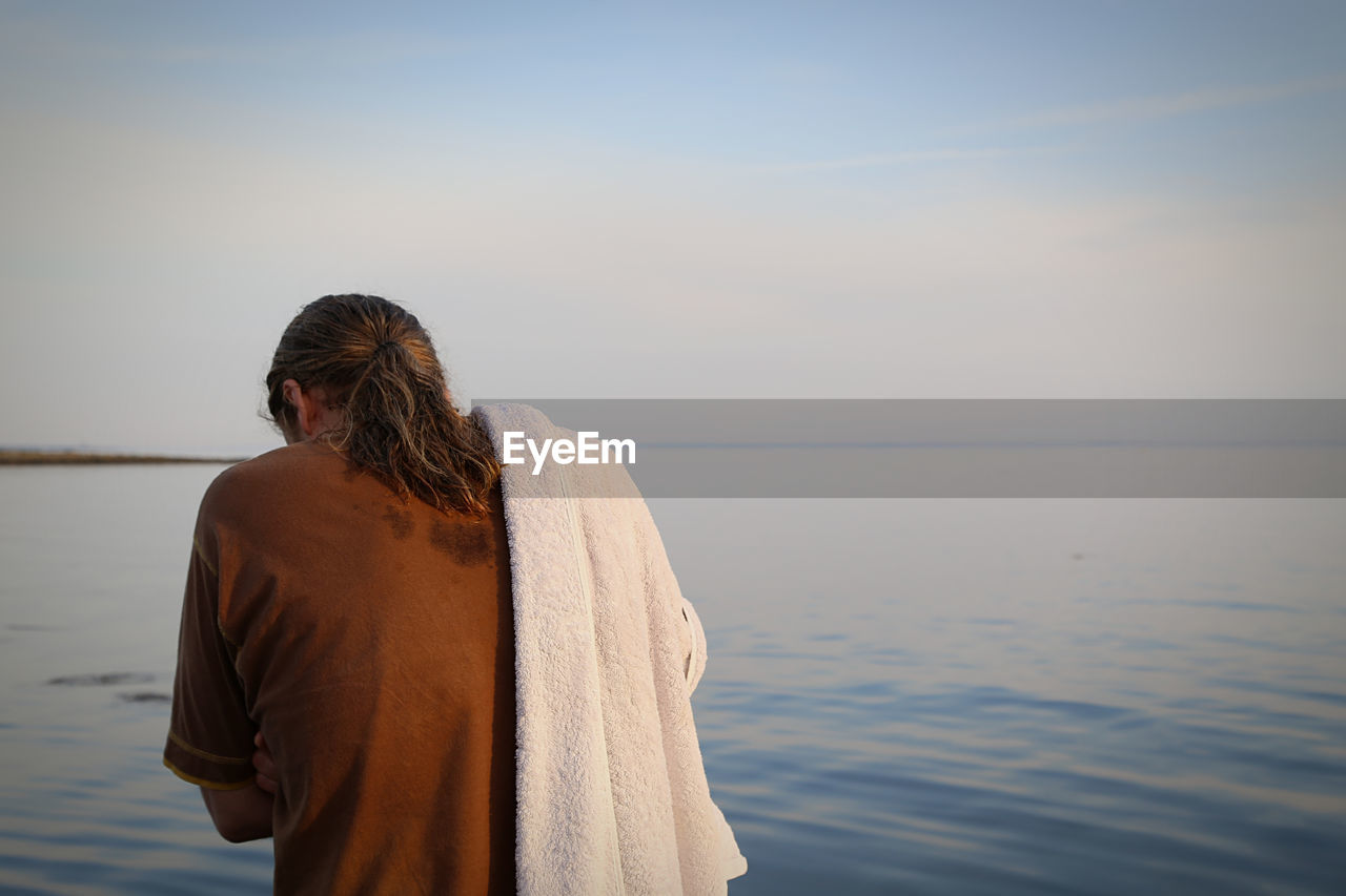 Rear view of man standing with towel by sea against sky