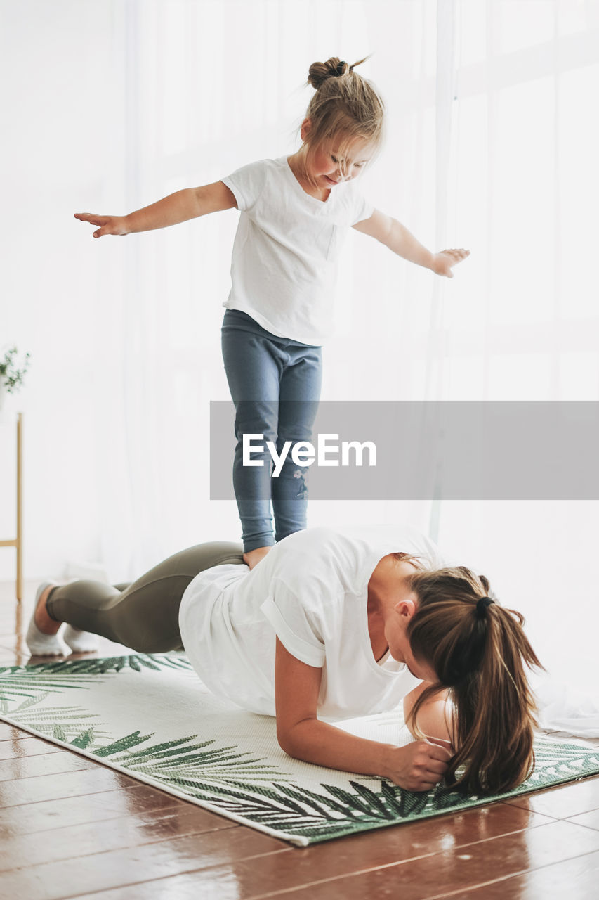 Girl standing on mother back exercising at home