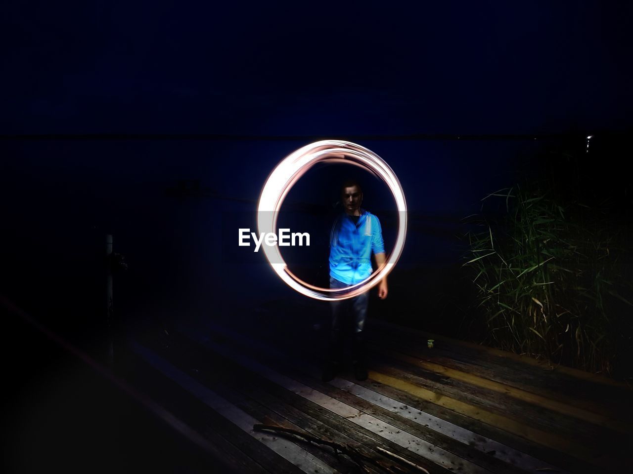 BLURRED MOTION OF MAN STANDING ON ILLUMINATED LAMP AT NIGHT