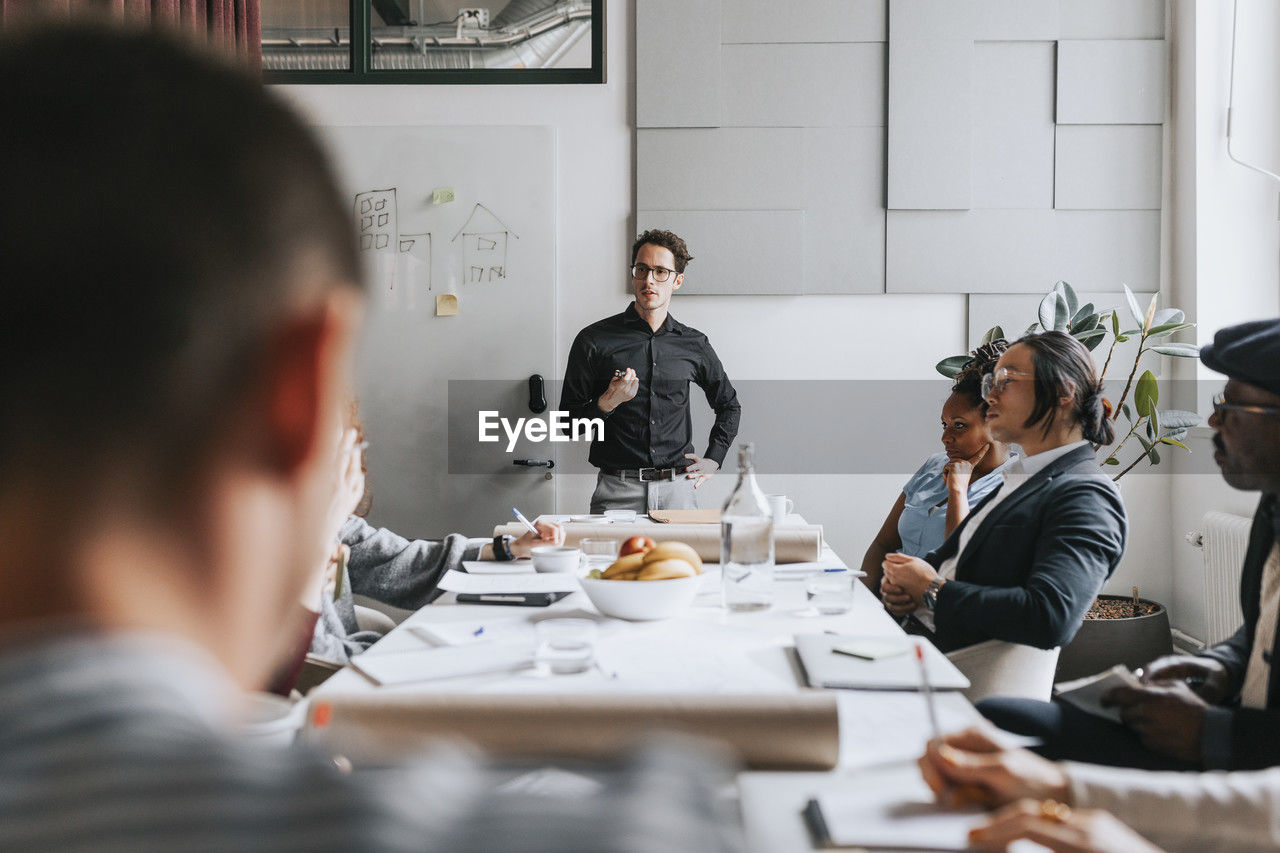 Businessman with hand on hip discussing with colleagues during meeting at office