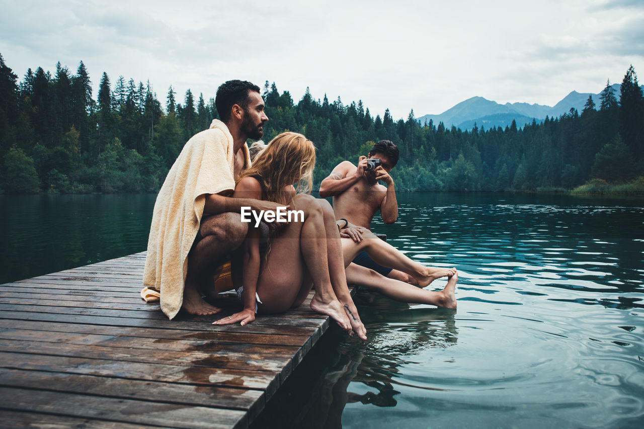 FRIENDS SITTING ON LAKE AGAINST SKY