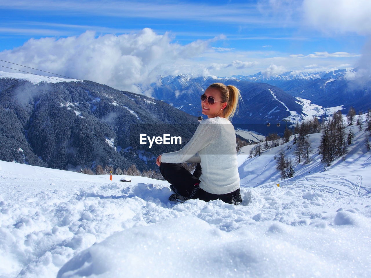 Portrait of young woman sitting on snow covered field against mountains