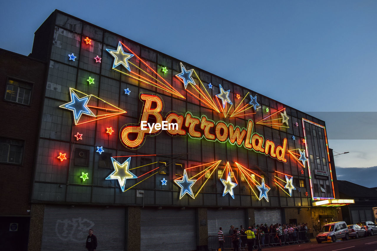 LOW ANGLE VIEW OF ILLUMINATED TEXT ON BUILDING AGAINST SKY AT NIGHT