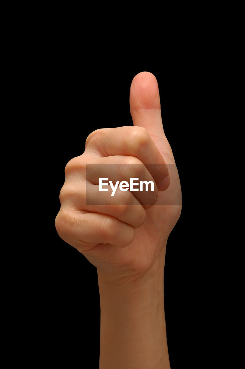 Close-up of hand showing thumbs up against black background