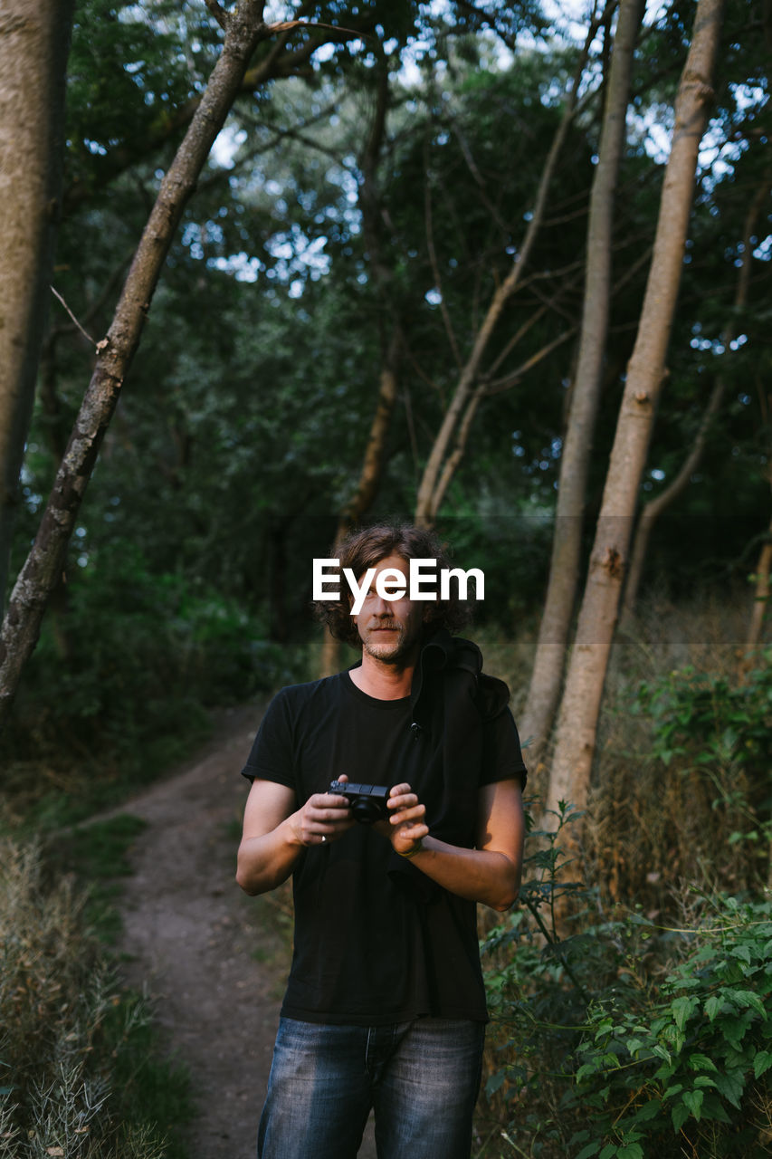 Portrait of young man using camera in forest