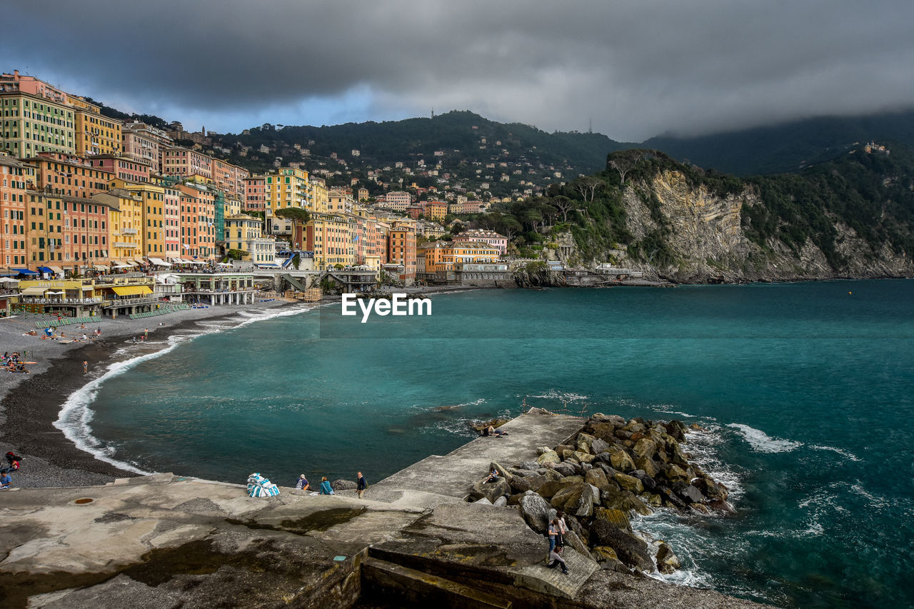 Scenic view of sea by buildings against cloudy sky