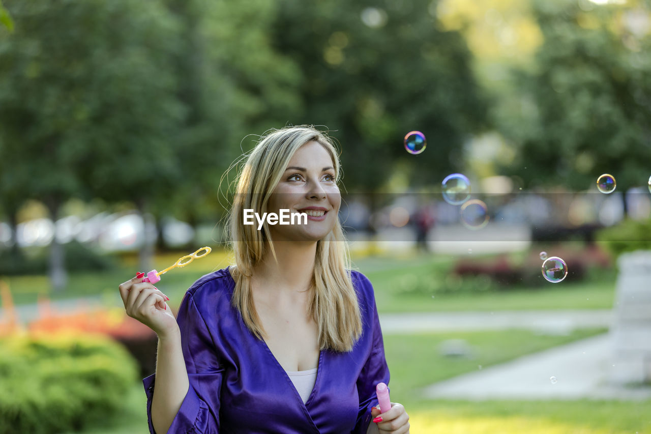 Beautiful blonde with long hair and long purple dress is balancing in public park. 