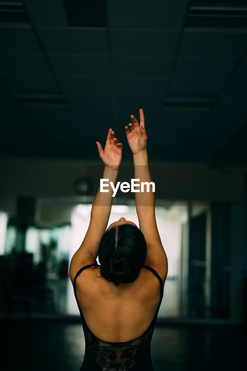 Rear view of woman with hands raised at dance studio