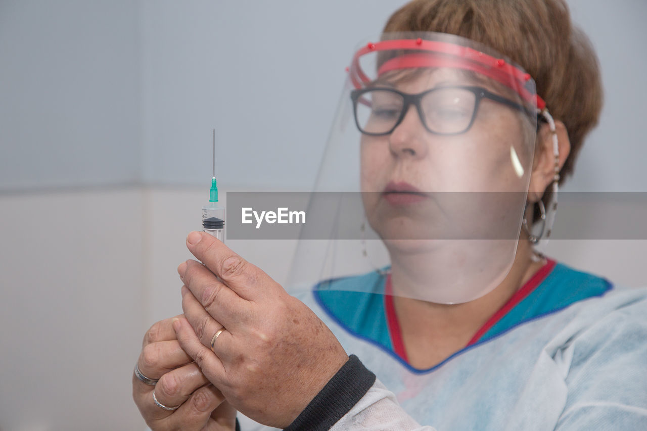 Close-up of doctor wearing face shield holding syringe