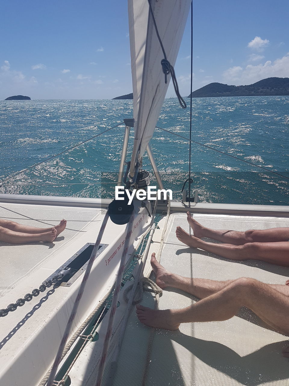 Low section of people relaxing on boat deck over sea against sky