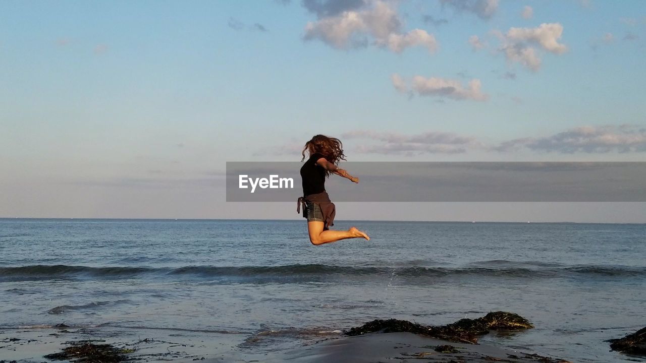 WOMAN JUMPING IN SEA AGAINST SKY