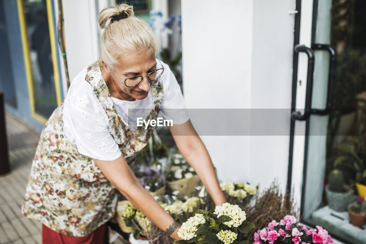 Blond female florist arranging flowers outside store
