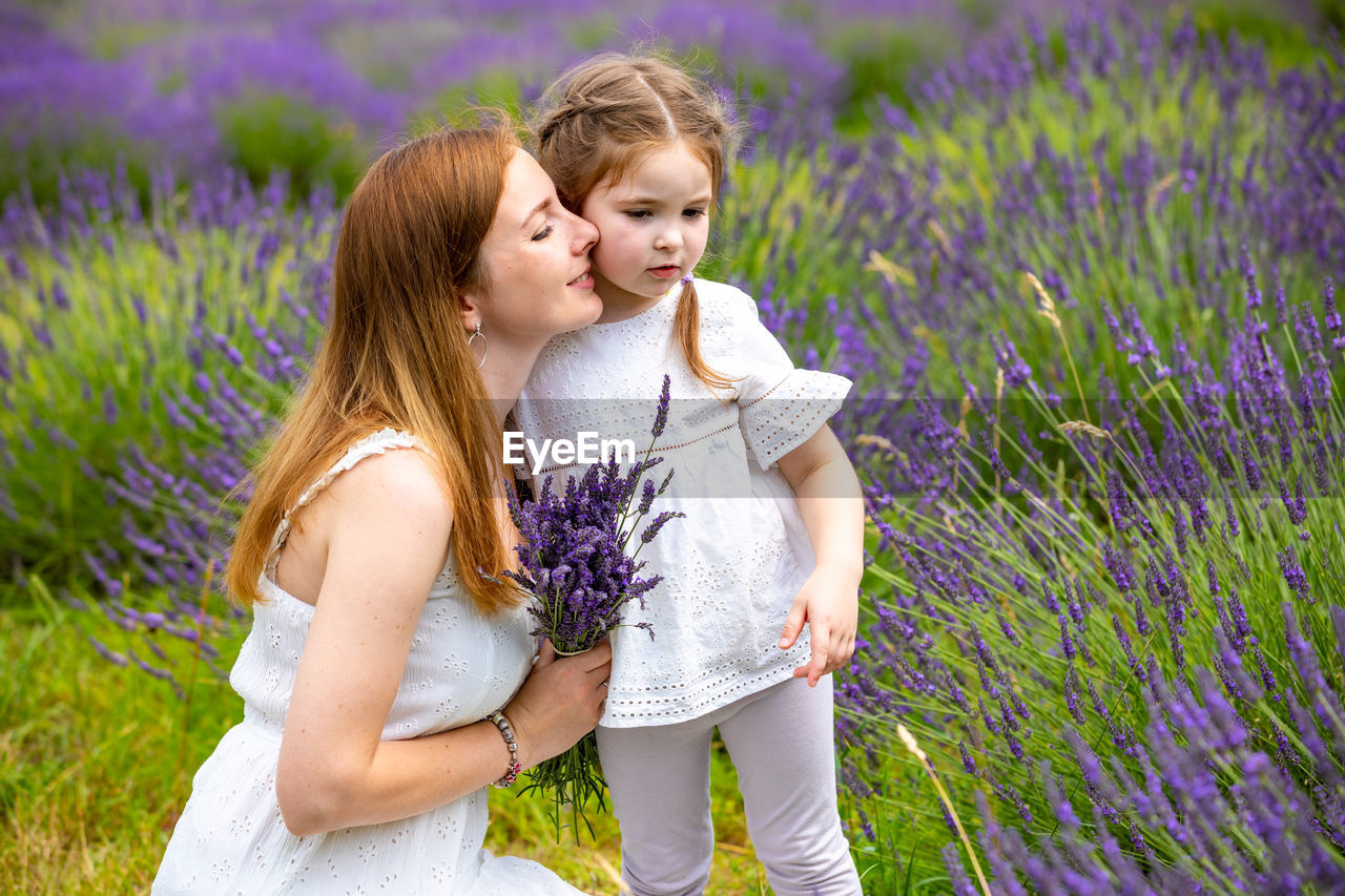 View of mother and girl by purple flowering plants on field