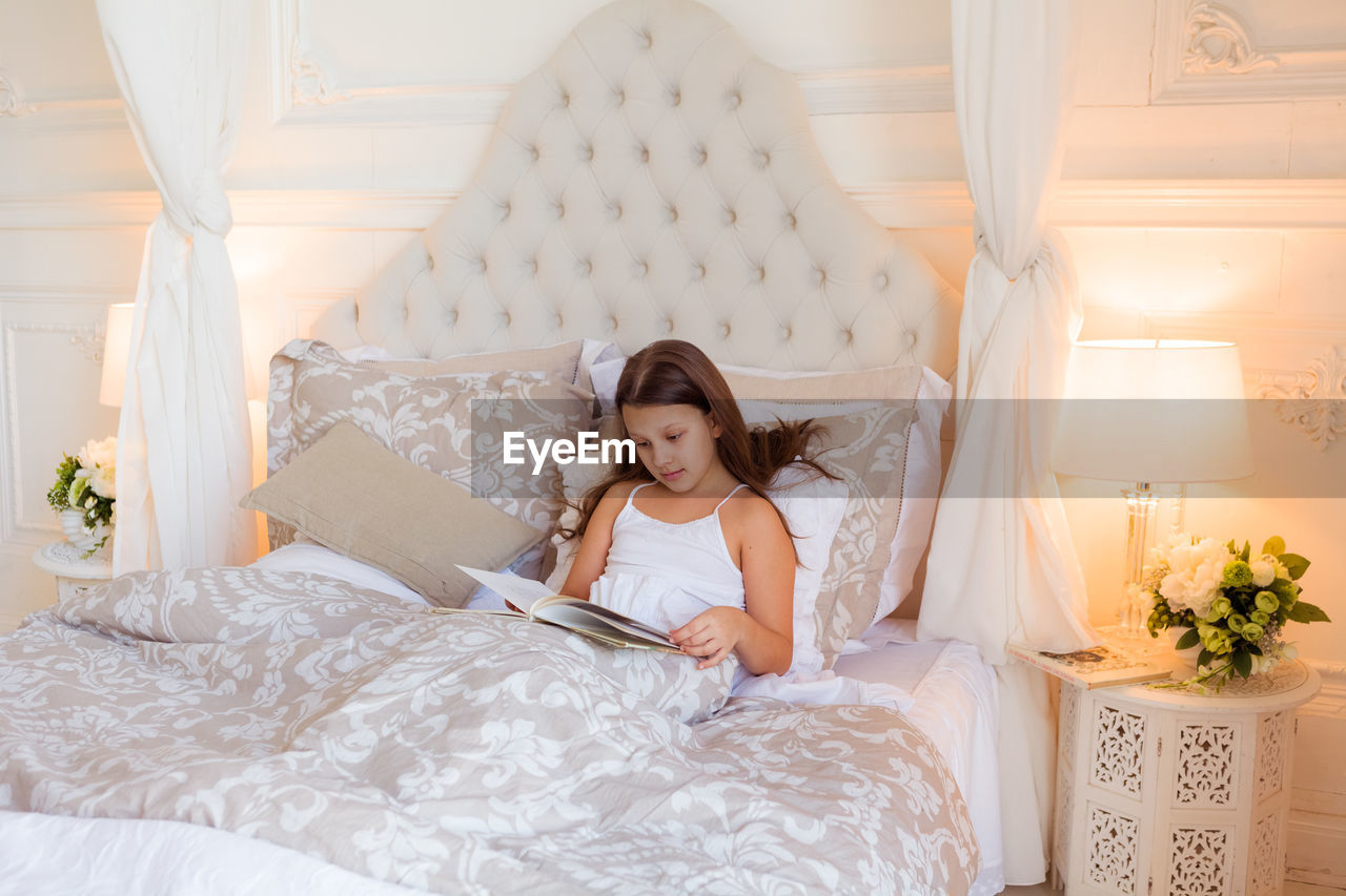 Smiling girl laying on bed in bedroom and reading a book