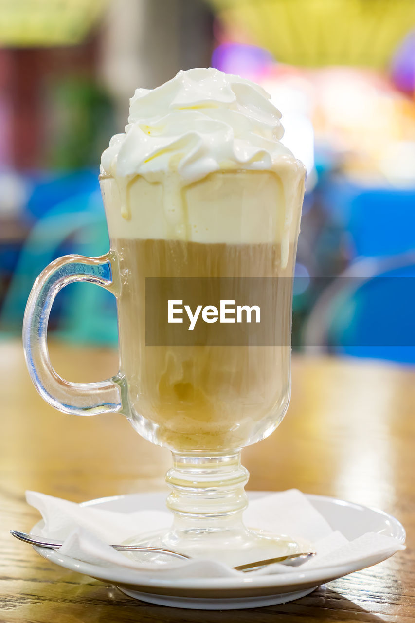 Glass cup of coffee latte with whipped cream on wooden table