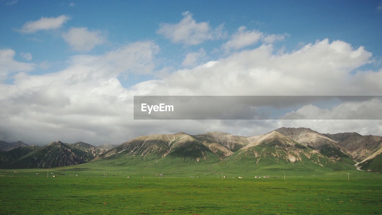 Scenic view of grassy field and mountain range against cloudy sky