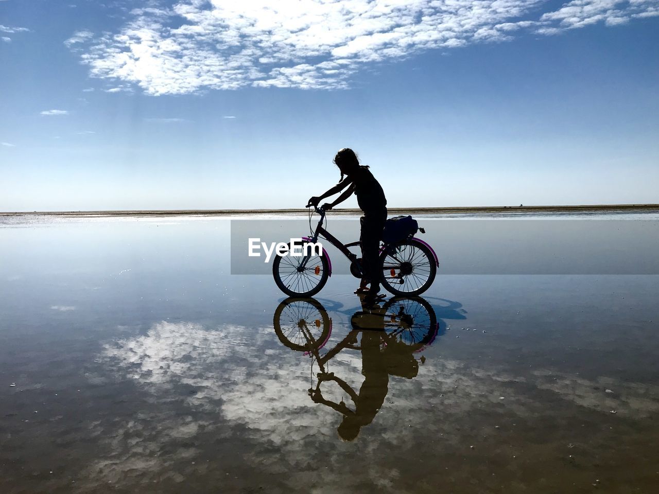 MAN RIDING BICYCLE ON SEA SHORE AGAINST SKY