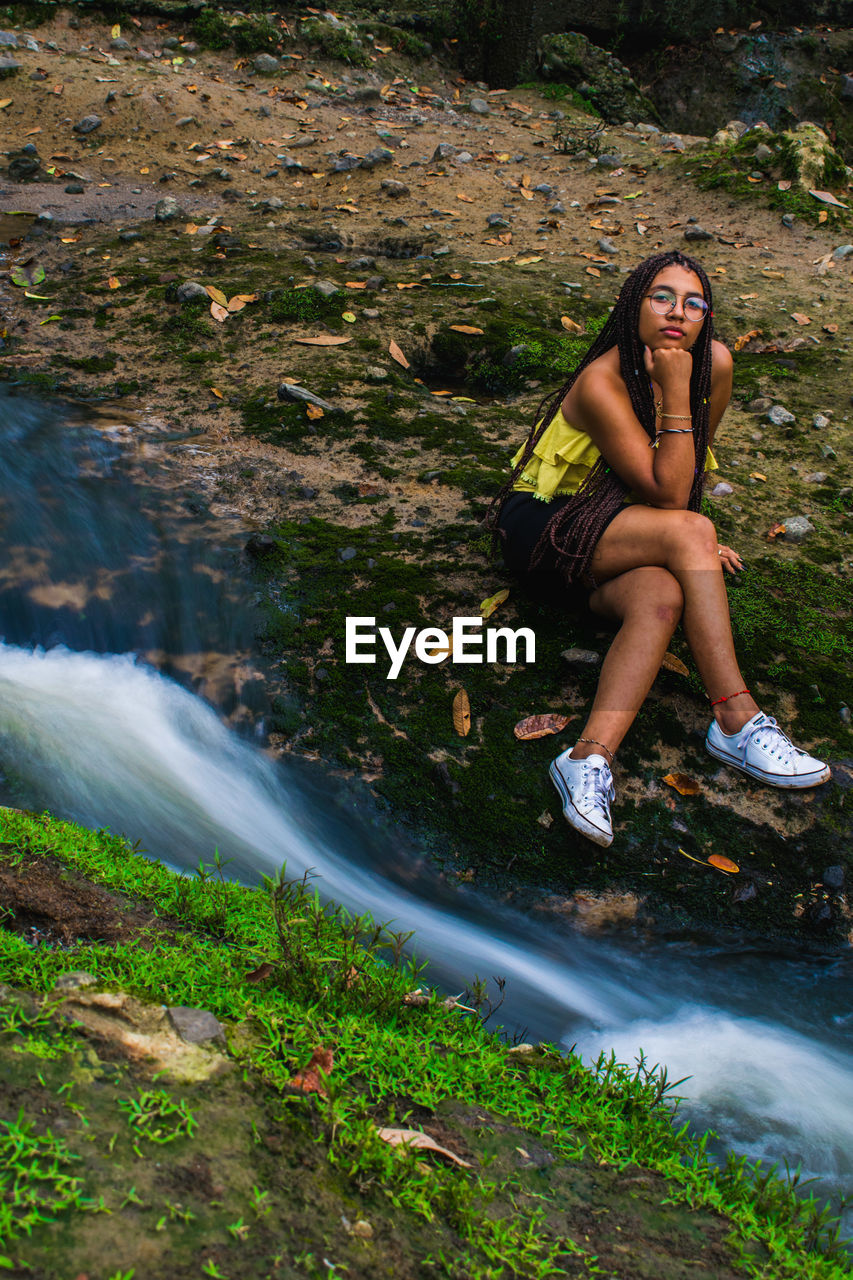 Portrait of teenage girl sitting by stream on field