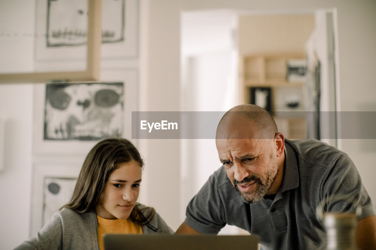 Father and daughter using laptop in kitchen at home