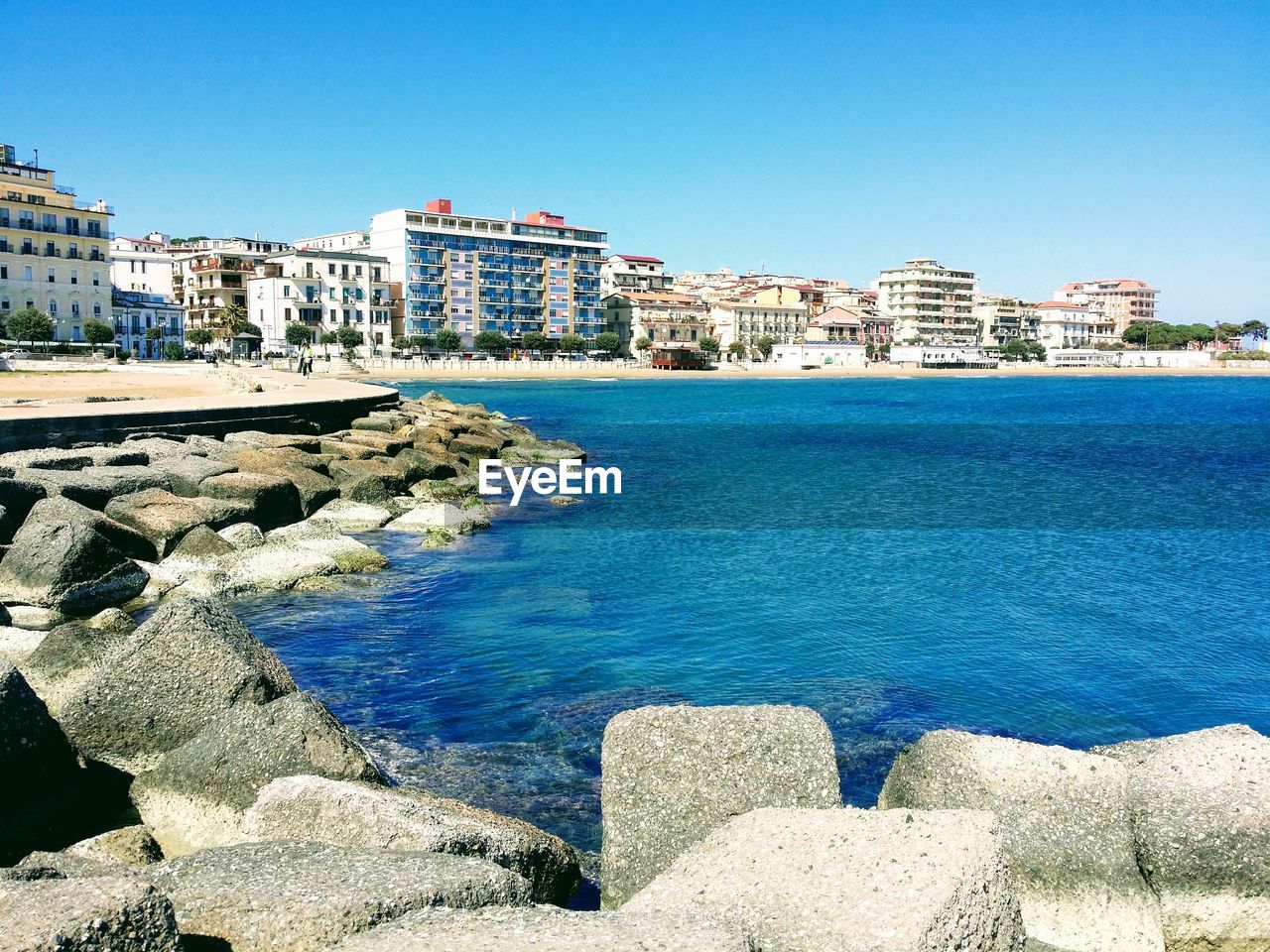 Buildings by sea against blue sky
