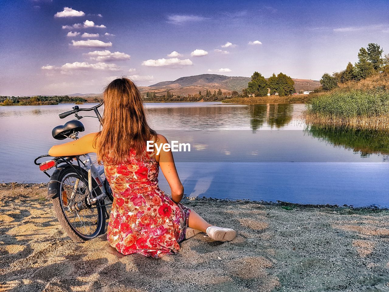 Rear view of woman sitting with bicycle on sand at lakeshore