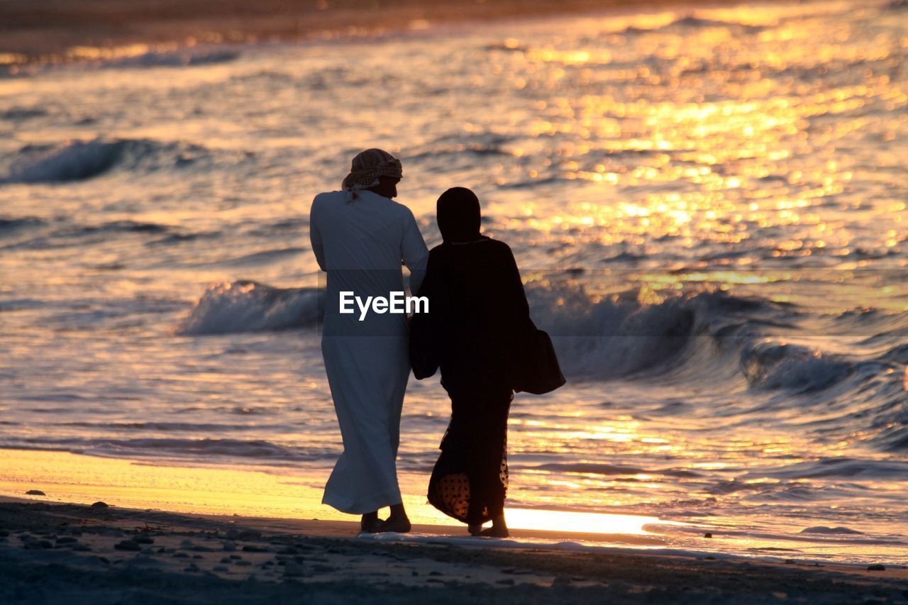 REAR VIEW OF COUPLE STANDING AT BEACH