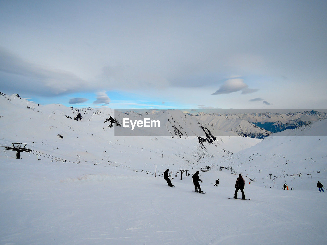 Silhouette people skiing on ski slope against cloudy sky