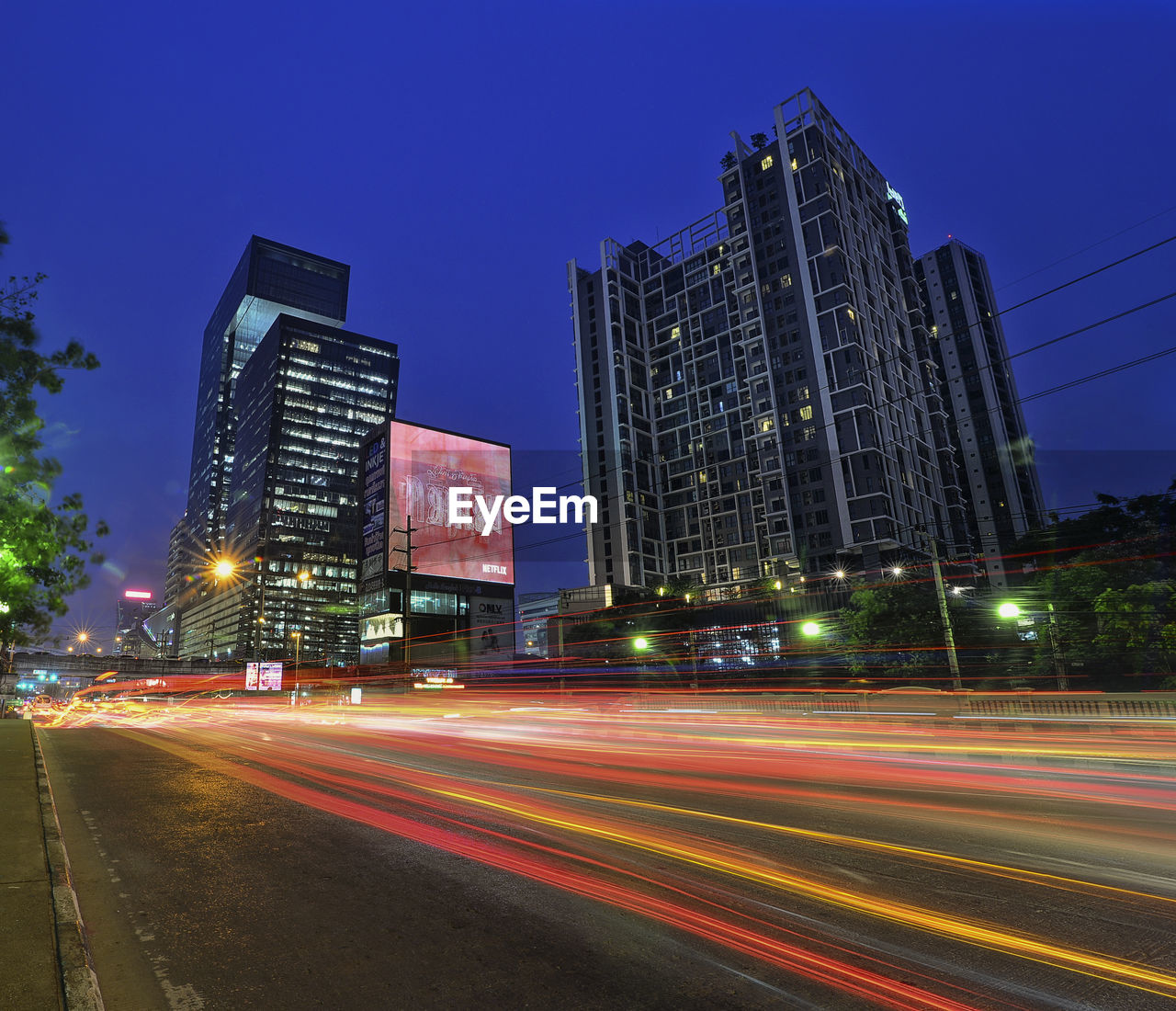 LIGHT TRAILS ON ROAD BY BUILDINGS AGAINST SKY