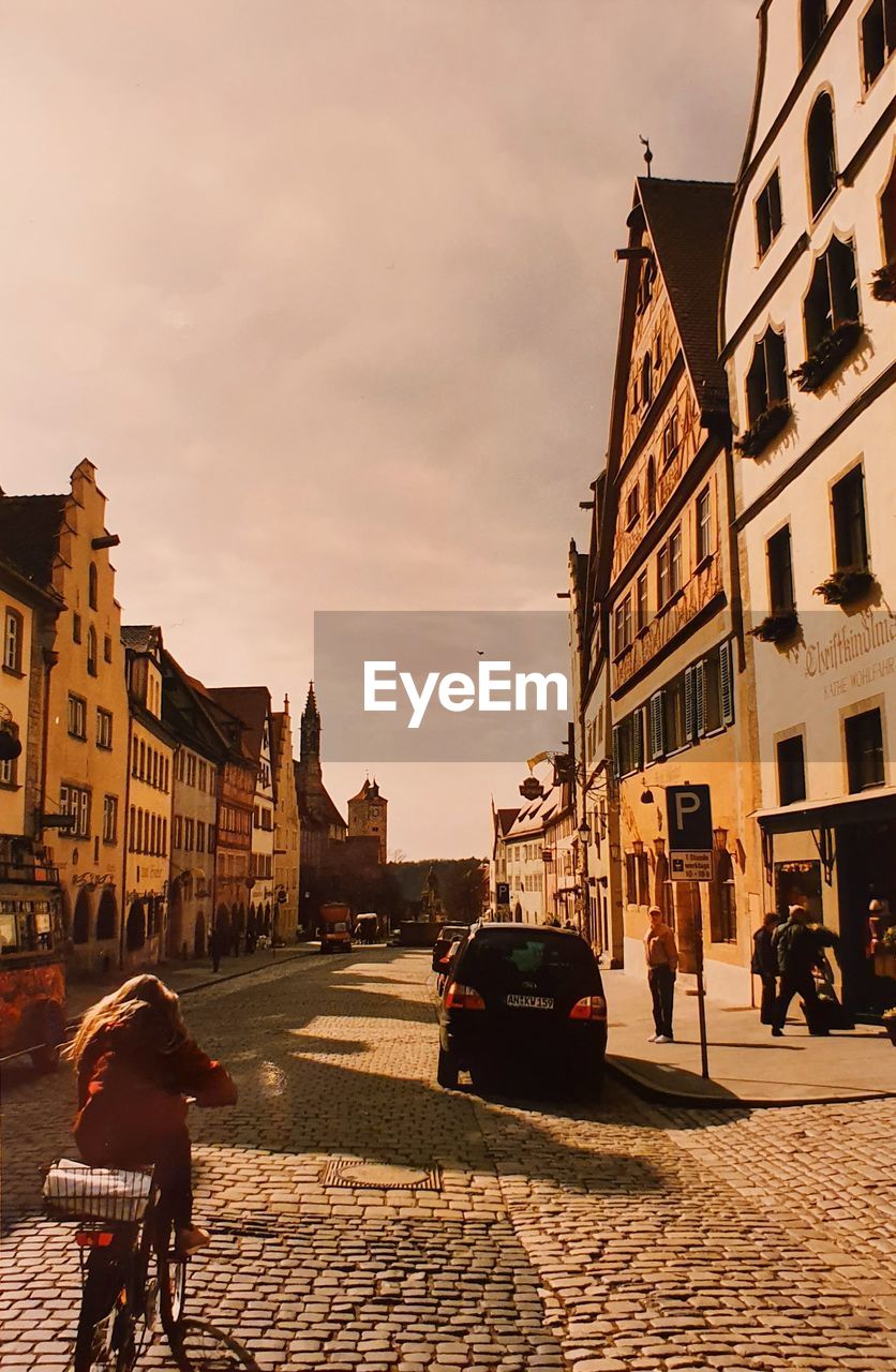 PEOPLE WALKING ON STREET BY BUILDINGS AGAINST SKY IN CITY