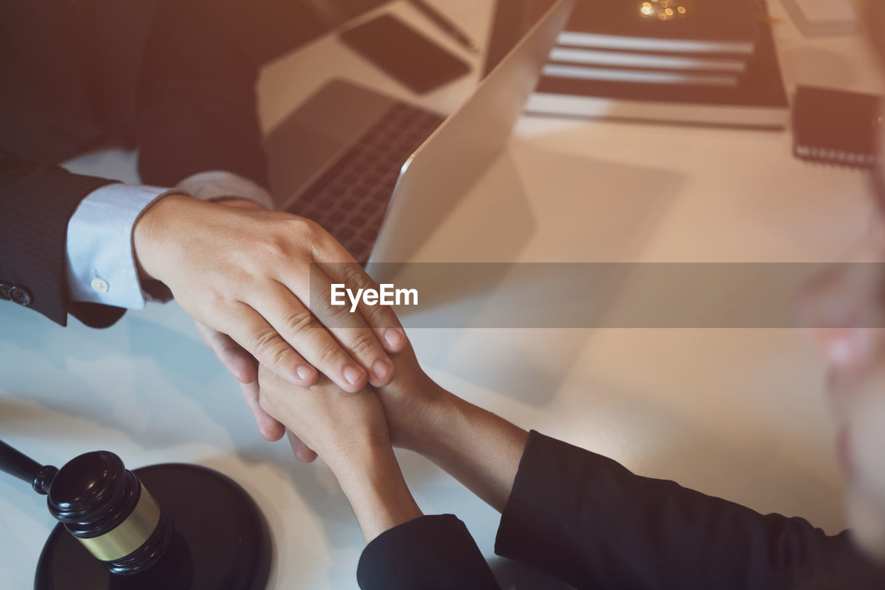 Cropped hands of lawyer holding client hands on desk