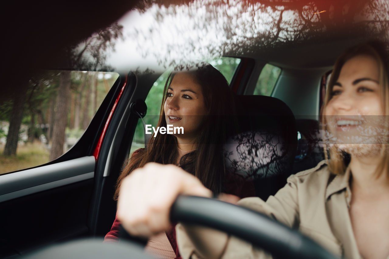 Smiling female friends looking away while traveling in car