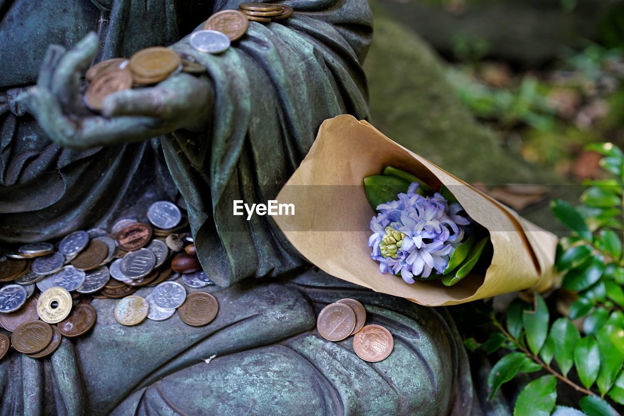 Close-up of statue with flowers and coins