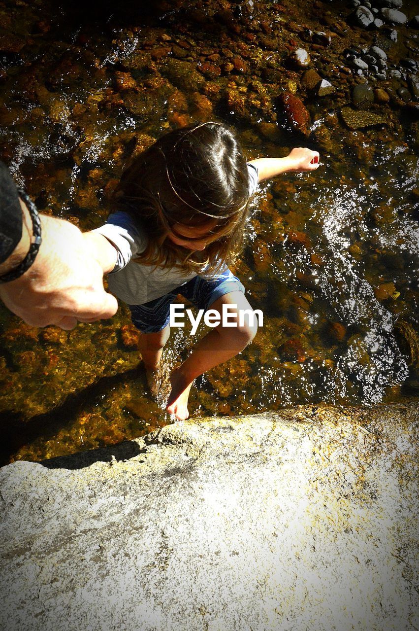 Cropped hand of father helping daughter to climb on rock by river