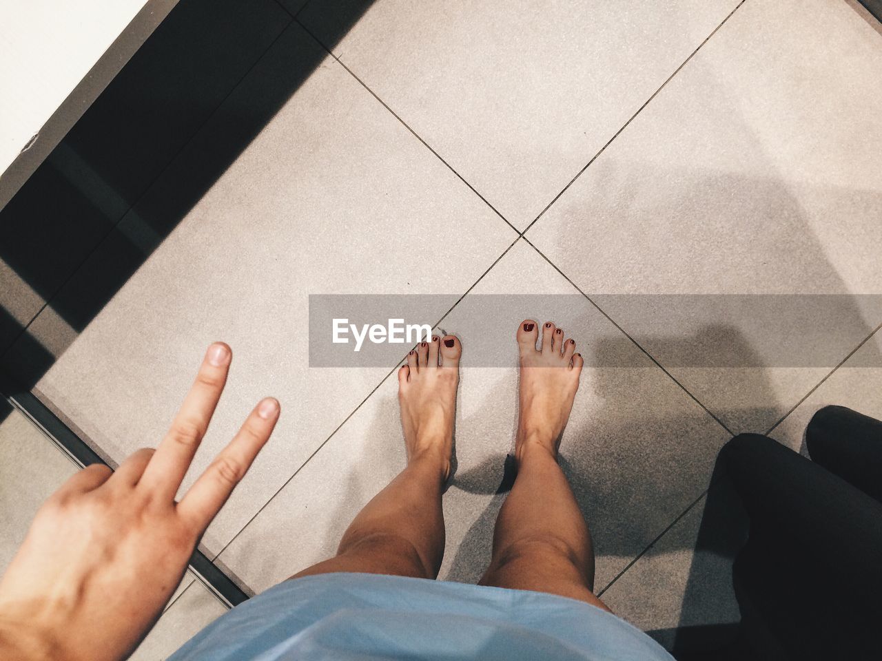 Low section of woman showing peace sign while standing on floor