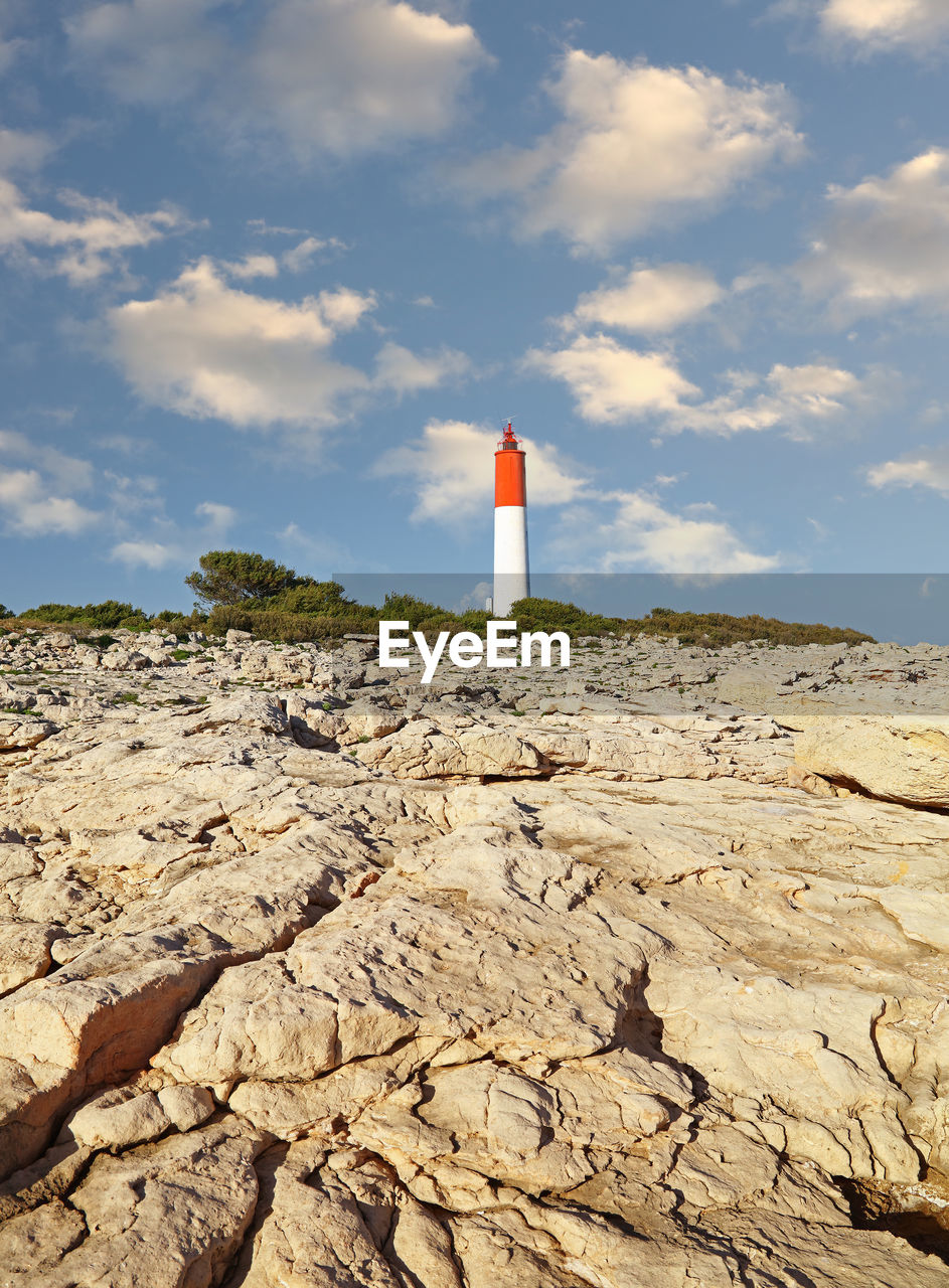 LIGHTHOUSE AND ROCKS ON BEACH AGAINST SKY