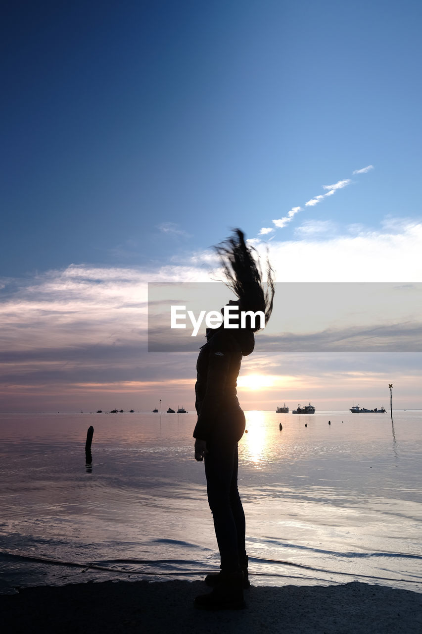 Silhouette woman standing on beach against sky during sunset