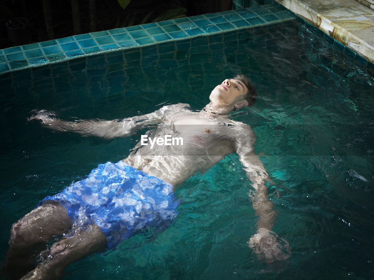 High angle view of shirtless young man swimming in pool
