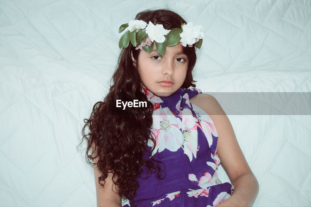 Portrait of girl wearing flowers while lying on bed at home