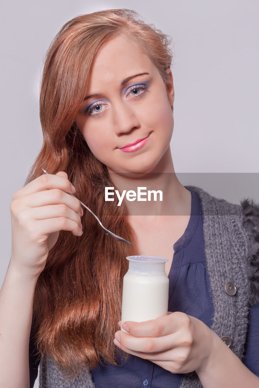 Portrait of beautiful young woman having milk against gray background