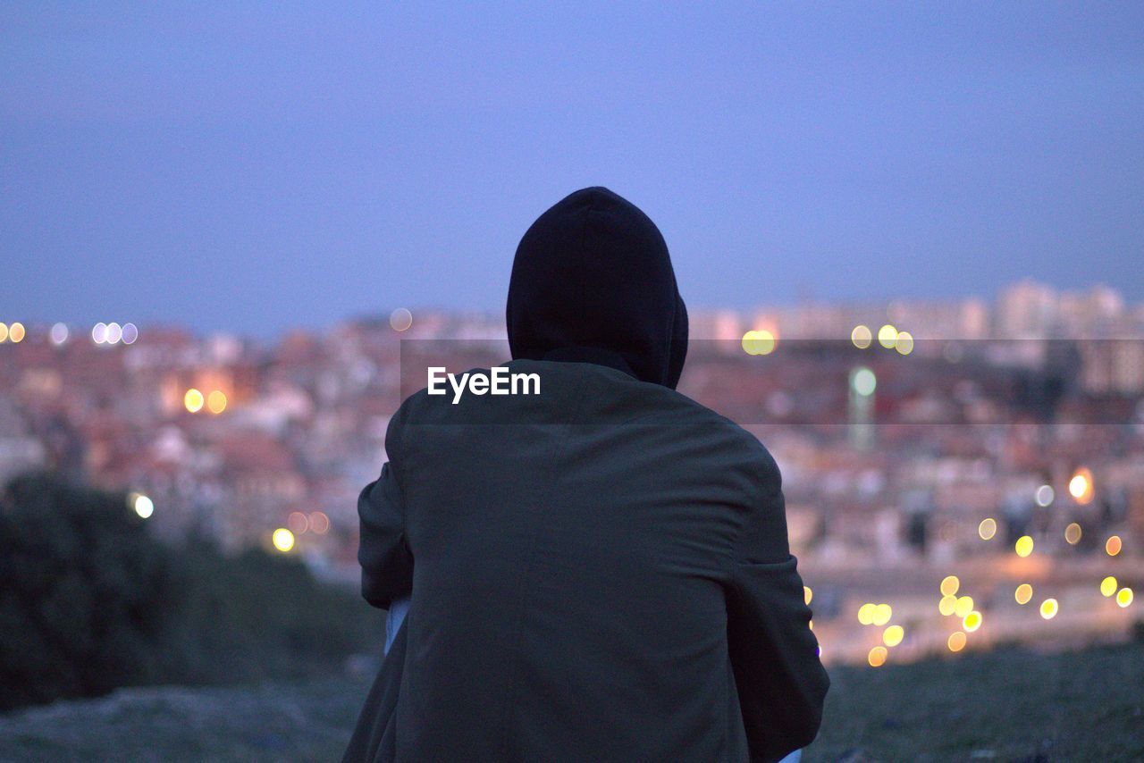 Rear view of man sitting against illuminated city