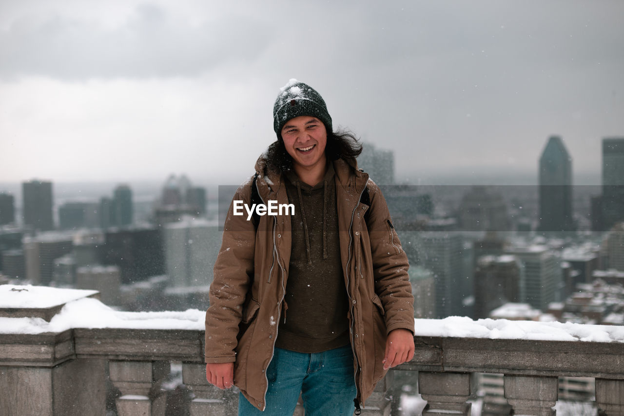 Portrait of smiling man standing against cityscape during winter
