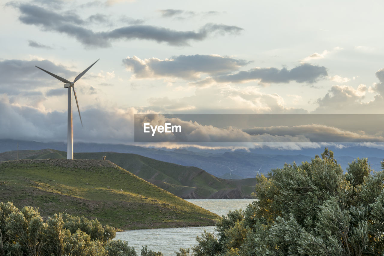 Wind power turbine on hill in front of cloudy sky