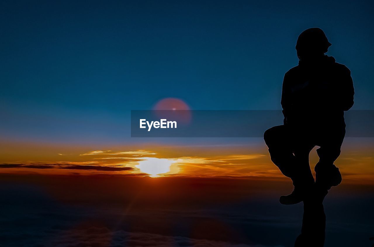 Silhouette man standing by sea against sky during sunset