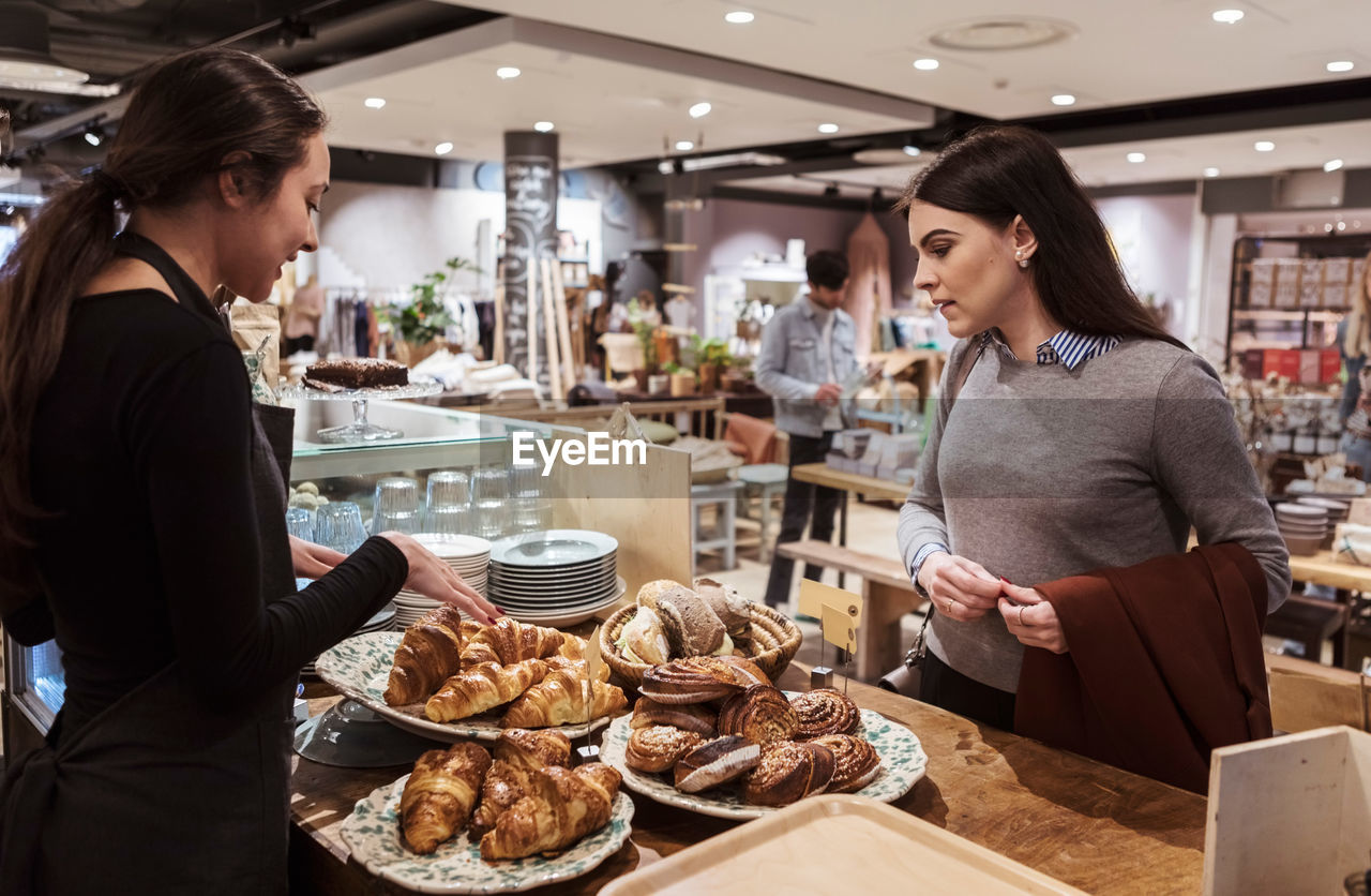 Saleswoman showing baked food to female customer at cafe