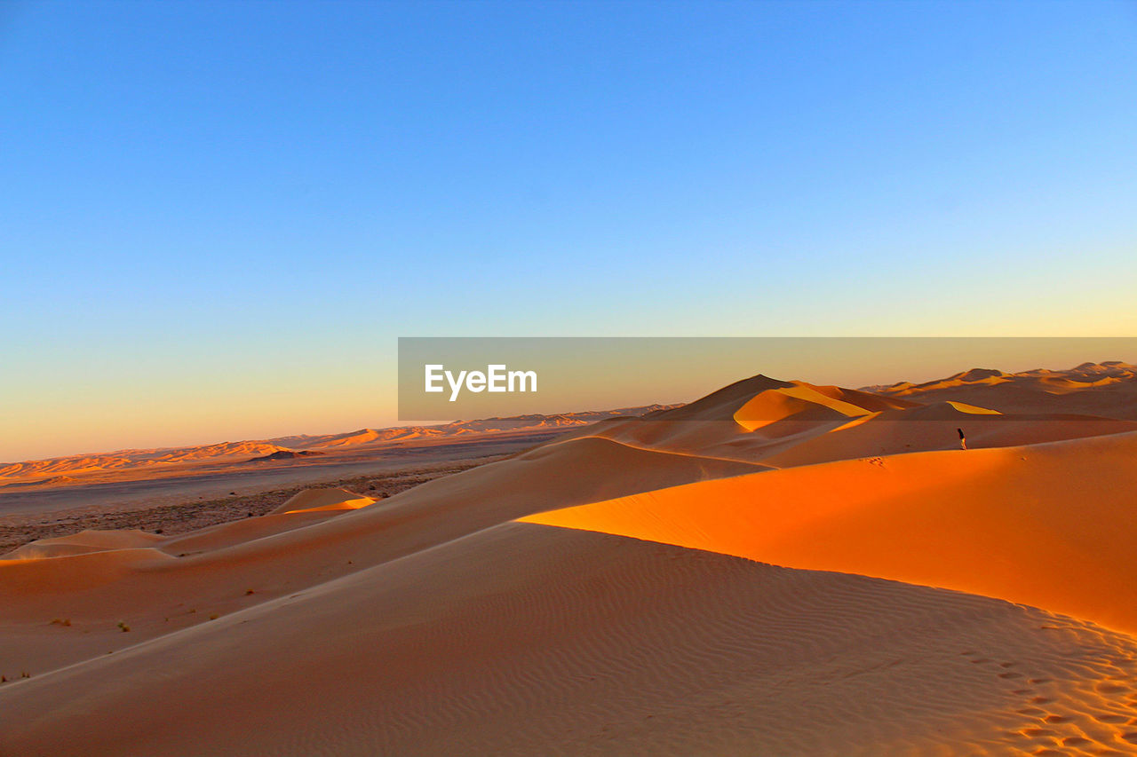 Scenic view of desert against clear sky at sunset