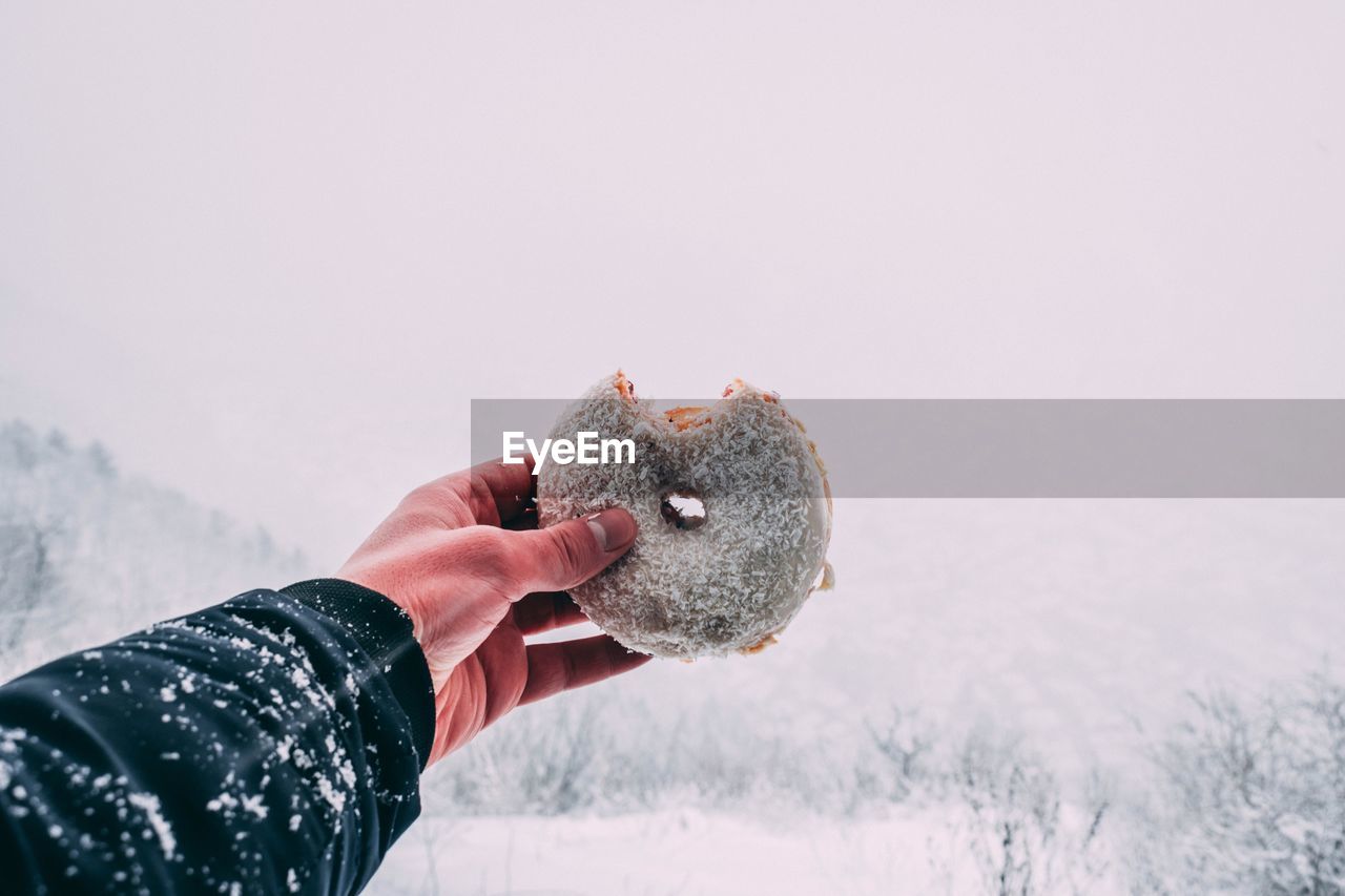 Close-up of hand holding donut against sky during winter