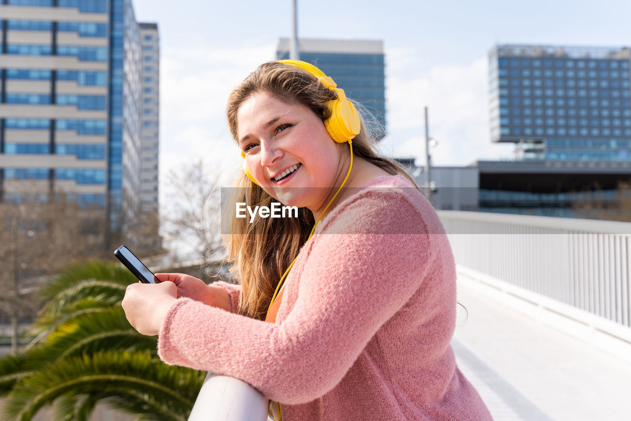 Young woman listening music against sky