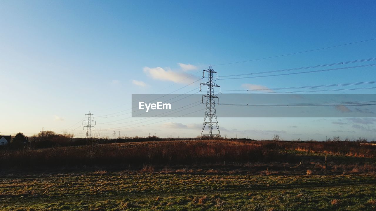 ELECTRICITY PYLONS ON FIELD AGAINST SKY