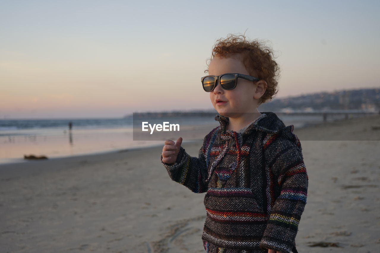 Boy standing on beach against sky during sunset